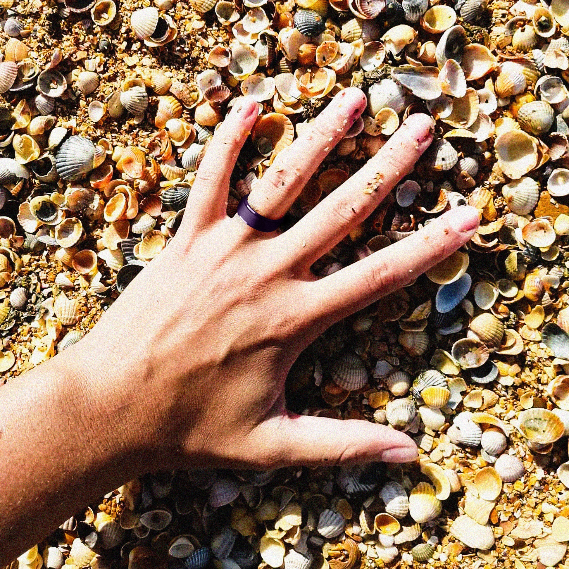 Woman’s hand wearing silicone ring on the beach with seashells