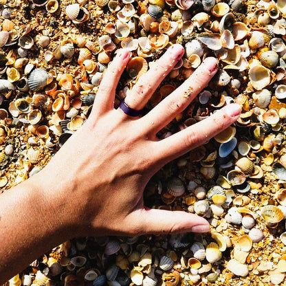 Woman’s hand wearing silicone ring on the beach with seashells